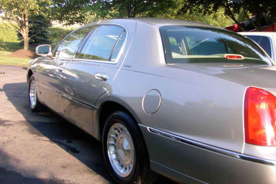 Silver full-size sedan, rear three-quarter view, parked outdoors near trees
