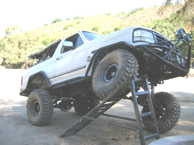 White lifted topless Ford Bronco with roll cage flexing on an RTI ramp, big mud tires and tube bumper
