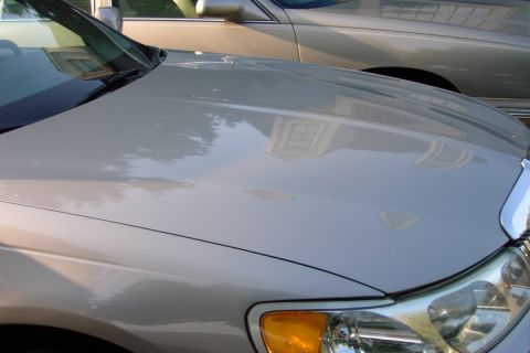 1996 Mercury Grand Marquis - A silver sedan's hood and headlight are visible, with a reflection of a house in the polished surface. Another car is parked alongside.