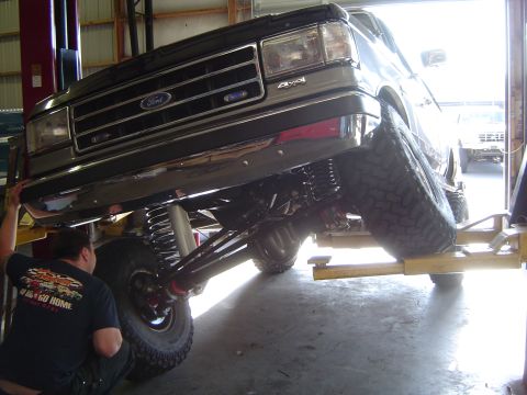 1989 Ford Bronco - A 1989 Ford Bronco is shown from the front, lifted on a service rack with visible suspension upgrades.