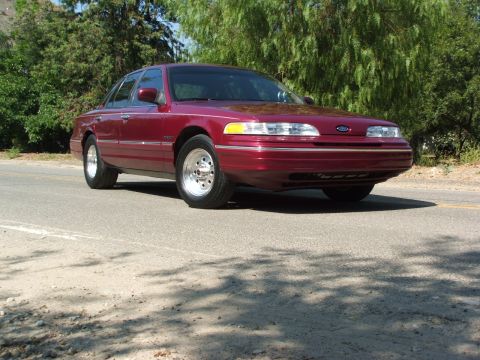 1992 Ford Crown Victoria - A maroon Ford Crown Victoria is parked on the side of a road with trees in the background.