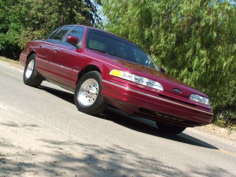 1992 Ford Crown Victoria - A maroon 1992 Ford Crown Victoria is viewed from a low angle on a tree-lined road.