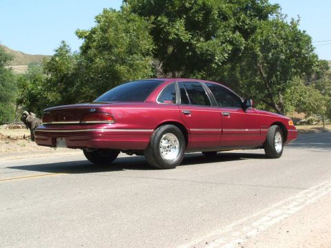 1992 Ford Crown Victoria - A red 1992 Ford Crown Victoria is seen from the rear 3/4 angle, aftermarket wheels and a fresh coat of paint.