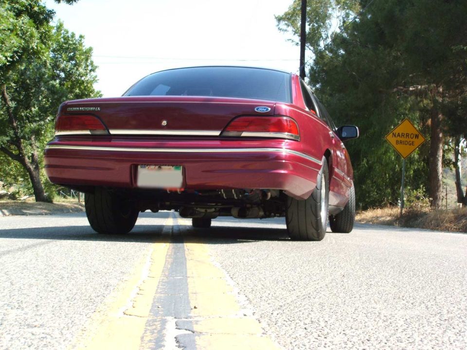 Ground-level rear view of a maroon Ford Crown Victoria LX sedan on a two-lane road