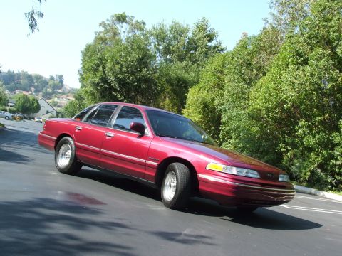 1992 Ford Crown Victoria - A red 1992 Ford Crown Victoria sedan is shown from a three-quarter front angle on a sunny day.