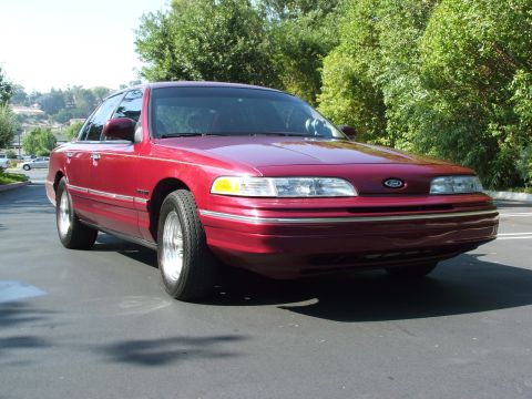 1992 Ford Crown Victoria - This 1992 Ford Crown Victoria is shown in a three-quarter front view, highlighting its red paint and classic sedan body style.