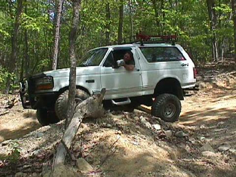 1996 Ford Bronco - A white 1996 Ford Bronco navigates a challenging off-road trail with a driver visible inside.