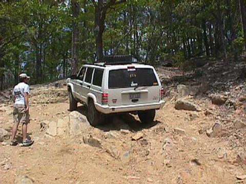 1996 Ford Bronco - A white SUV navigates a challenging, rocky off-road trail. The Supermotors.net logo is visible in the lower right corner.