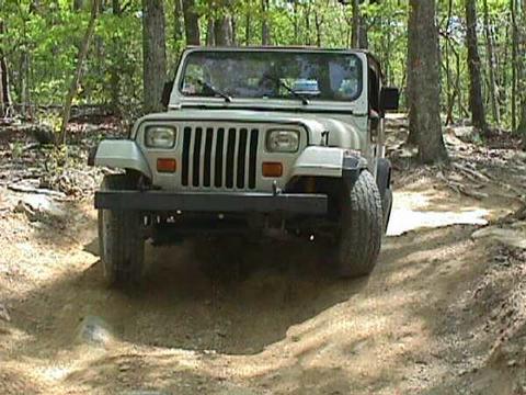 1996 Ford Bronco - A Jeep Wrangler navigates a rough, wooded trail.
