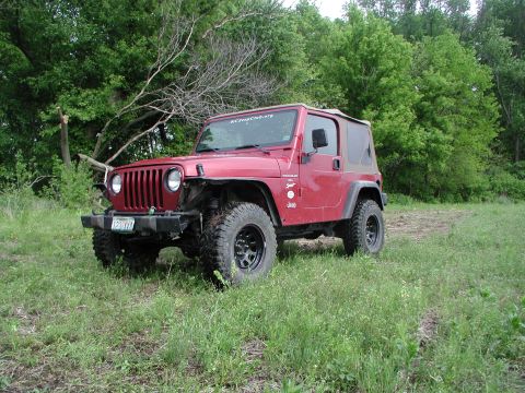 1998 Jeep TJ - A red 1998 Jeep TJ is seen from a 3/4 front view, parked in a grassy area with trees in the background.