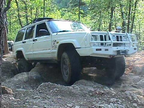 1996 Ford Bronco - A white Jeep Cherokee XJ navigates a challenging rocky trail with a modified front bumper.