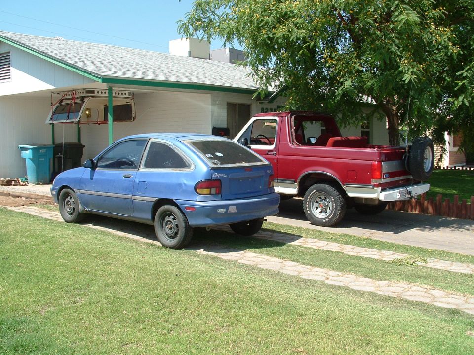 Blue Ford Aspire hatchback beside maroon Ford Bronco in a driveway