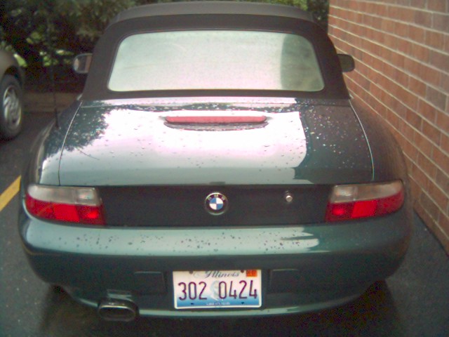 Rear view of dark green BMW Z3 convertible with black soft top and Illinois plate 302 0424 by brick wall