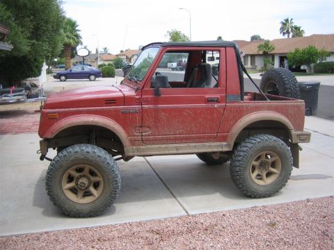 1987 Suzuki Samurai - This red 1987 Suzuki Samurai is parked on a driveway, showing its lifted suspension and off-road tires.