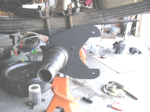 1994 Ford Bronco - A close-up view of a vehicle's disc brake assembly, supported by an orange jack stand, with leaf springs visible overhead.