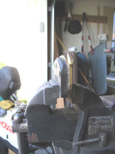1994 Ford Bronco - A metal bracket, likely for a disc brake caliper, is secured in a heavy-duty vise in a workshop setting.
