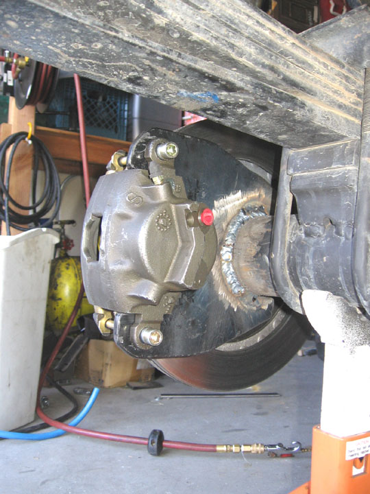 Rear disc brake caliper mounted on a rotor with visible welds on the bracket