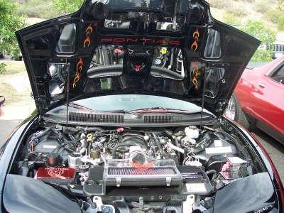 1972 Ford Ranchero - The engine bay of a black Pontiac is displayed, with a red car visible to the right.