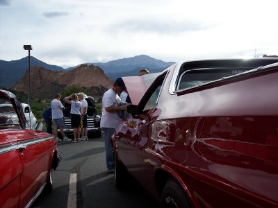 1972 Ford Ranchero - A group of people gather around a red 1972 Ford Ranchero with its hood open, set against a backdrop of mountains.