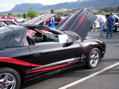 1972 Ford Ranchero - A black Pontiac Firebird Trans Am with red racing stripes is displayed with its hood open at an outdoor car show.