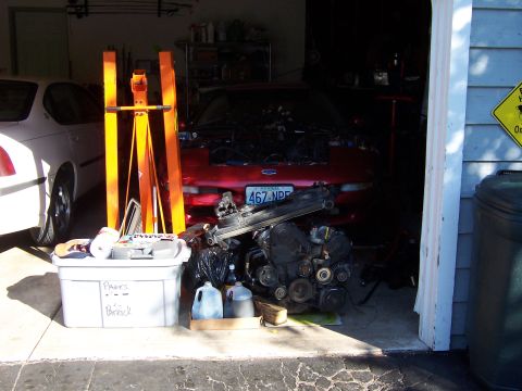 1996 Ford Probe - A red car sits in a garage with its engine removed, next to a white car and various parts.