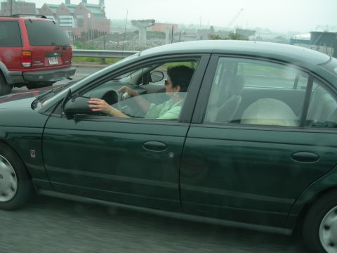 1992 Ford Taurus - Rolling side shot taken from another vehicle of a dark green Saturn sedan in traffic, with a driver in sunglasses at the wheel and a Saturn…