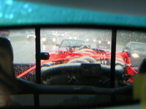 1992 Ford Taurus - View backward through a rain-beaded rear window with a green tint band, showing a large engine assembly secured under bright red ratchet st…