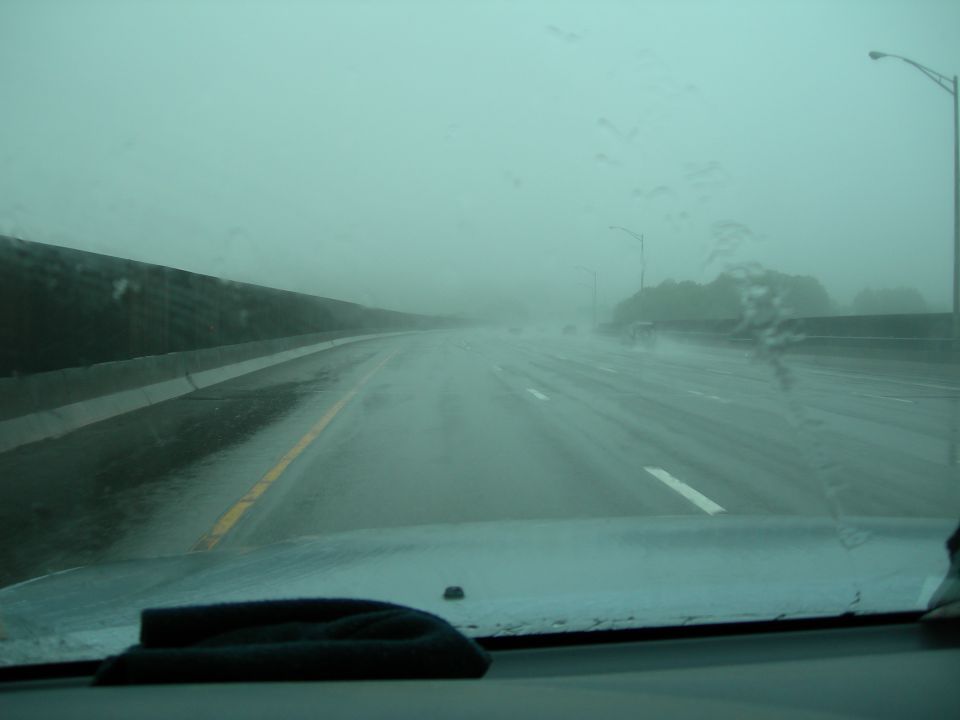 View through a rain-covered windshield of a multi-lane highway in heavy rain