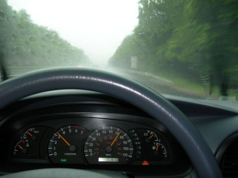 1992 Ford Taurus - Over-the-wheel shot of an analog instrument cluster in the rain, with the tach near 3,000 rpm, the needle around 70 mph on a 110 mph speedo…