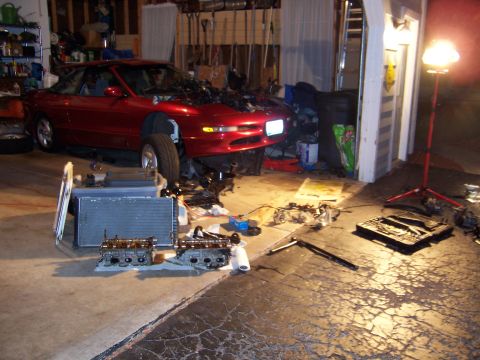 1996 Ford Probe - A red coupe is parked in a garage with its hood open and engine components disassembled and laid out on the floor.