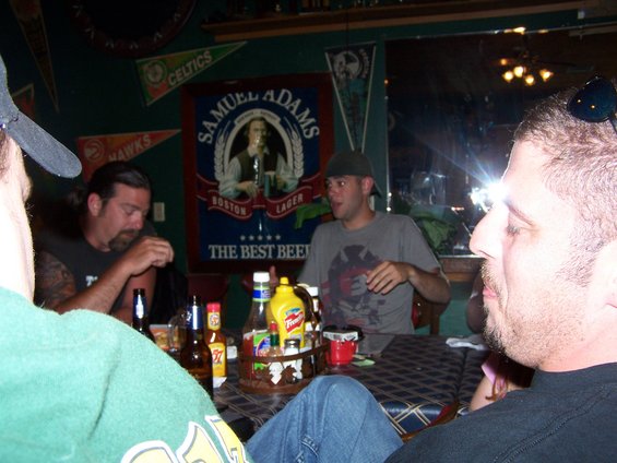 Guys sitting around a table with beer and condiments. A Samuel Adams sign is on the wall