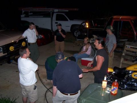 1995 Ford Bronco - A group of people are gathered around a beige truck at night, with other vehicles visible in the background.