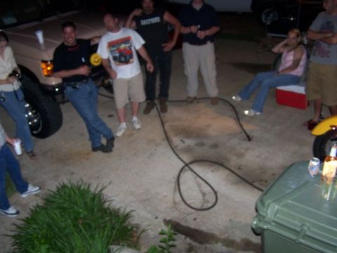 1995 Ford Bronco - A group of people are gathered around a tan SUV in a driveway at dusk.