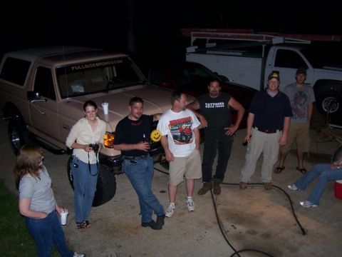 1995 Ford Bronco - A group of people stand around a tan Ford Bronco and a white pickup truck at night.