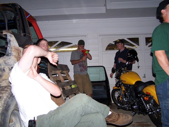 People gathered in a garage with a yellow motorcycle parked near garage doors