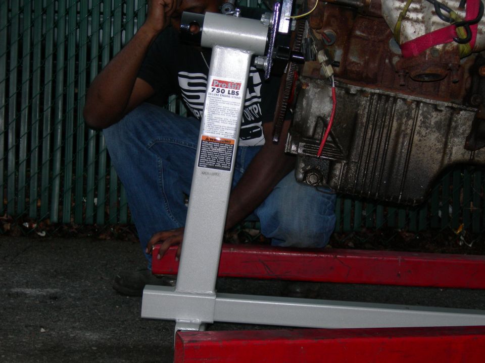 V6 engine block being mounted on a Pro-Lift 750 lb engine stand beside a red hoist