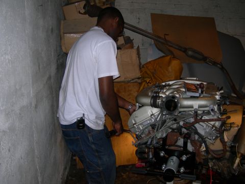 1992 Ford Taurus - A person in a white T-shirt and jeans works on a V6 engine mounted to a black engine stand in a cluttered basement, the polished tubular in…