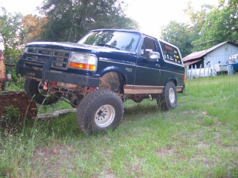 1995 Ford Bronco - This lifted Ford Bronco sits on a grassy field, its off-road tires and suspension clearly visible.