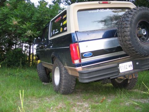 1995 Ford Bronco - This 1995 Ford Bronco features a dark blue body with a tan removable top and a spare tire mounted on the rear tailgate.