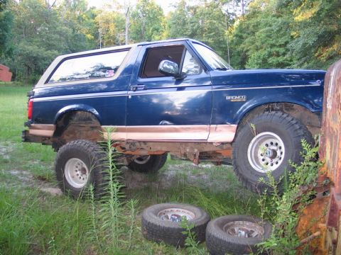 1995 Ford Bronco - Side view of a modified blue 1995 Ford Bronco with large tires and lifted suspension.