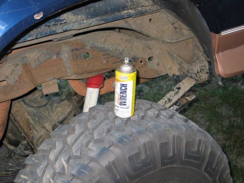1995 Ford Bronco - A can of Wrench Penetrant sits on a large tire, near the rusty frame and suspension of a vehicle.