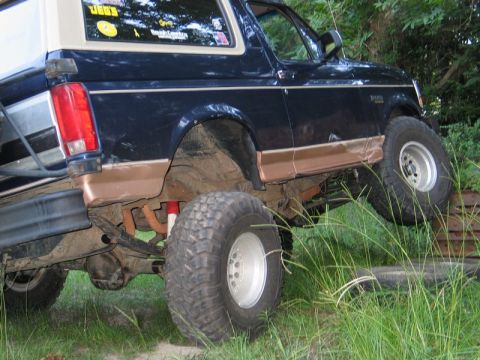 1995 Ford Bronco - Ford Bronco with aftermarket modifications, including large tires and suspension lift, navigating rough ground.