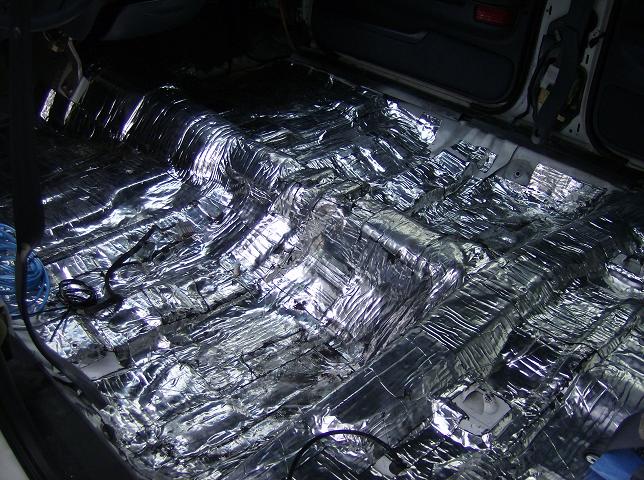 Car floor covered in shiny sound deadening material, wires visible
