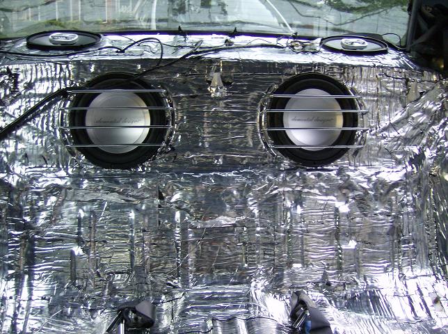 Two subwoofers with chrome grilles in a foil sound-deadened sedan rear deck
