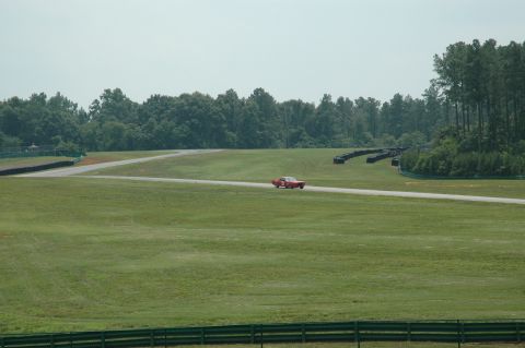 2000 Ford Mustang - A red sports car navigates a turn on a race track on a hazy day.