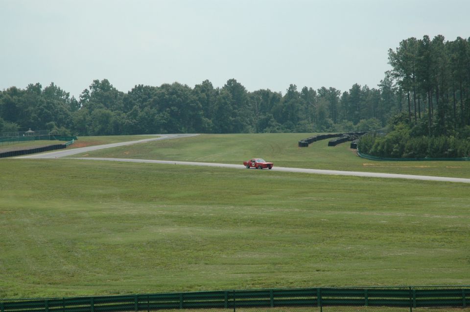 Red sports car driving on a paved race track with grassy infield and trees in background
