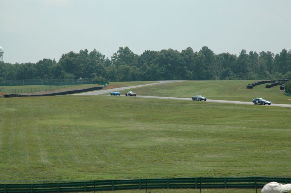 Four vintage race cars on a track with green grass and trees in the background
