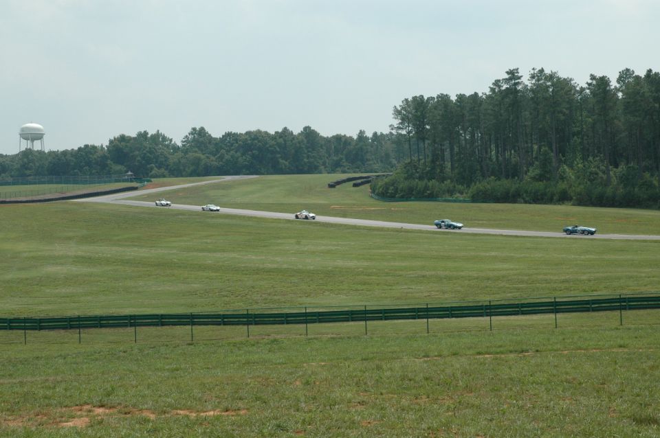 Several race cars on a track with a water tower and trees in the background