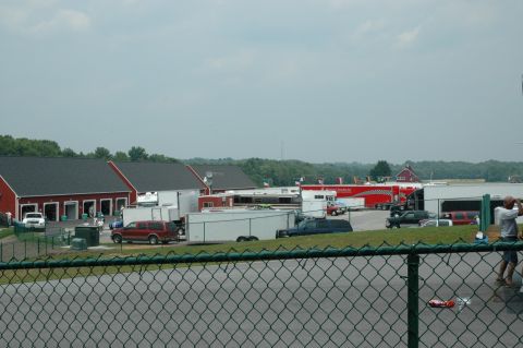 2000 Ford Mustang - A busy race track pit area with multiple buildings, trailers, and vehicles visible.