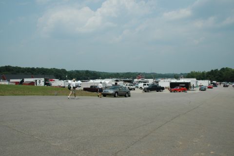 2000 Ford Mustang - A wide shot captures a busy outdoor event with numerous vehicles and structures under a partly cloudy sky.